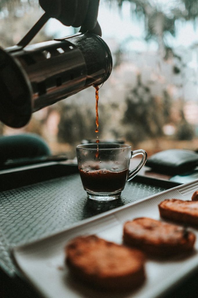pexels-photo-2748537 Aromatic coffee being poured into a glass cup beside a plate of biscotti on a tray.